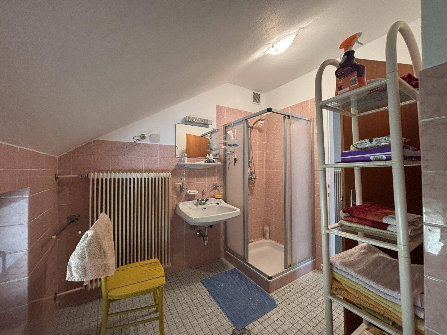 Badezimmer im Dachgeschoss mit Dusche, Waschbecken und rosa Fliesen im 80er-Jahre-Stil.