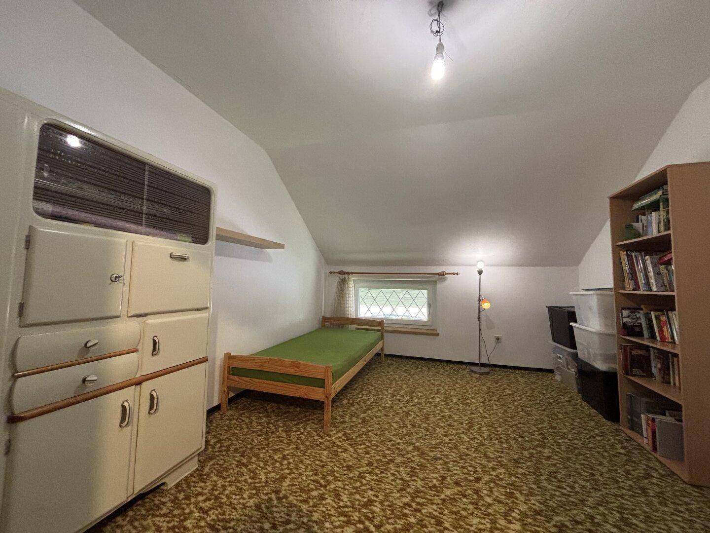 Schlafzimmer im Dachgeschoss mit Teppichboden, Einzelbett und kleinem Fenster.