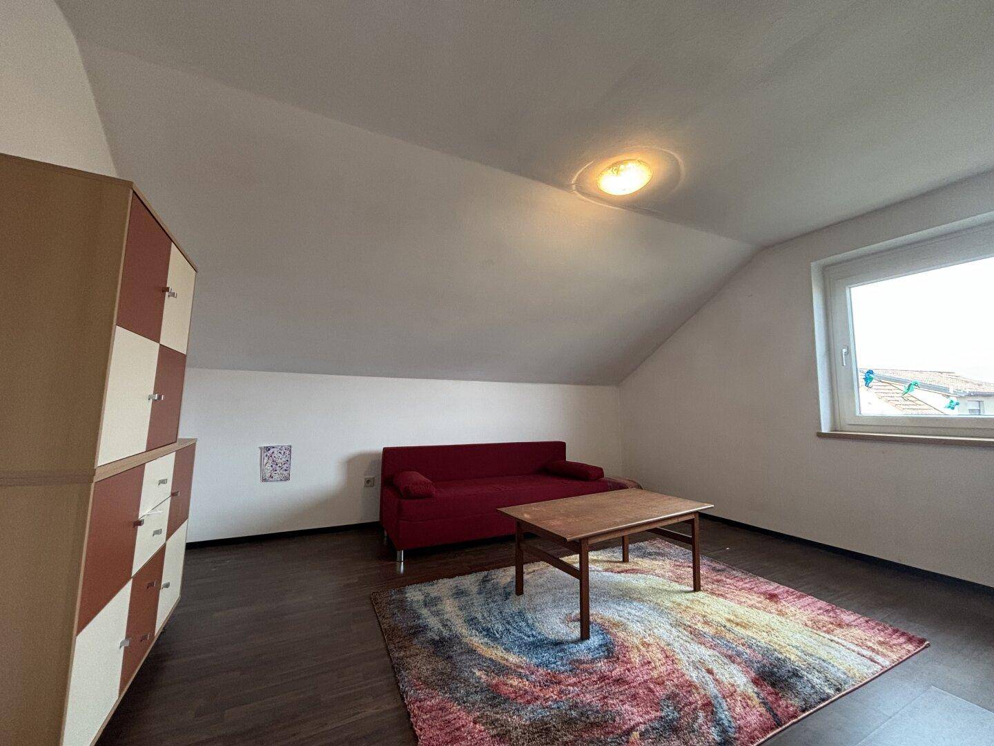 Wohnzimmer im Dachgeschoss mit rotem Sofa, Couchtisch und farbenfrohem Teppich.