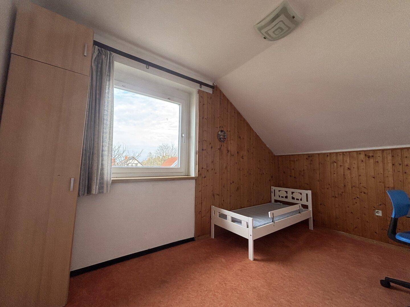 Kinderzimmer im Dachgeschoss mit Holzwandverkleidung, Einzelbett und Fenster.