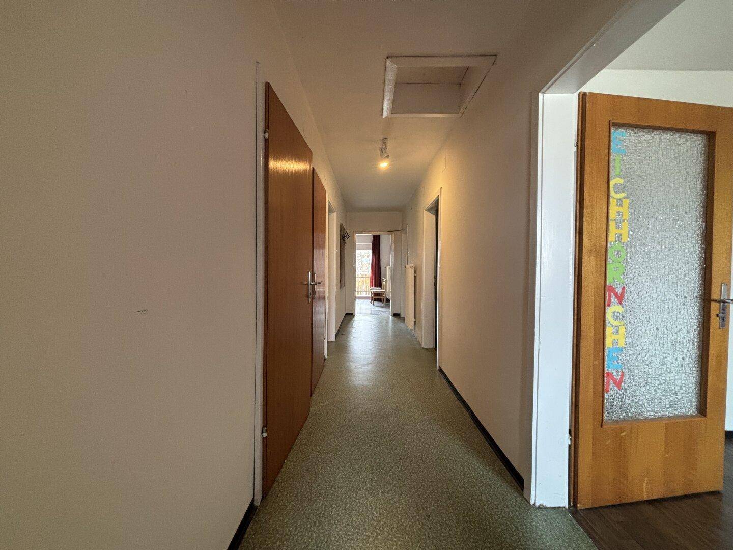 Langer Flur mit Linoleumboden und Holztüren, der zu verschiedenen Räumen führt.