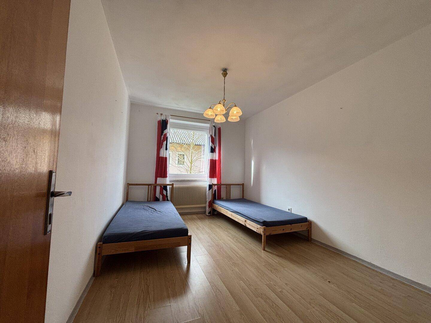 Schlafzimmer mit zwei Einzelbetten, Holzfußboden und einem Fenster mit Blick ins Grüne.