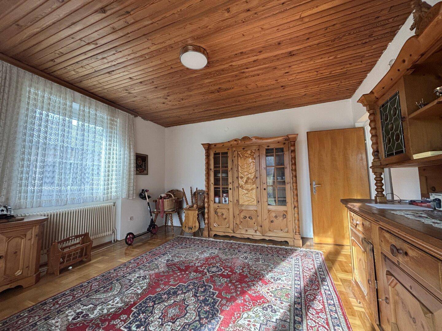 Gemütliches Wohnzimmer mit Holzbalkendecke, Teppich und traditionellen Holzmöbeln.