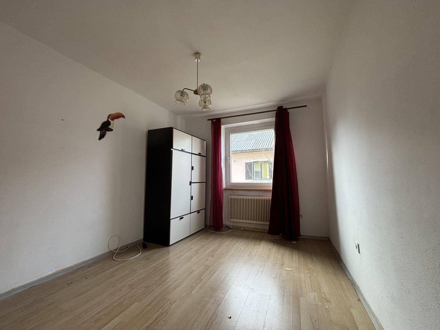 Schlafzimmer mit Laminatboden, Fenster und einem Kleiderschrank in Schwarz-Weiß.