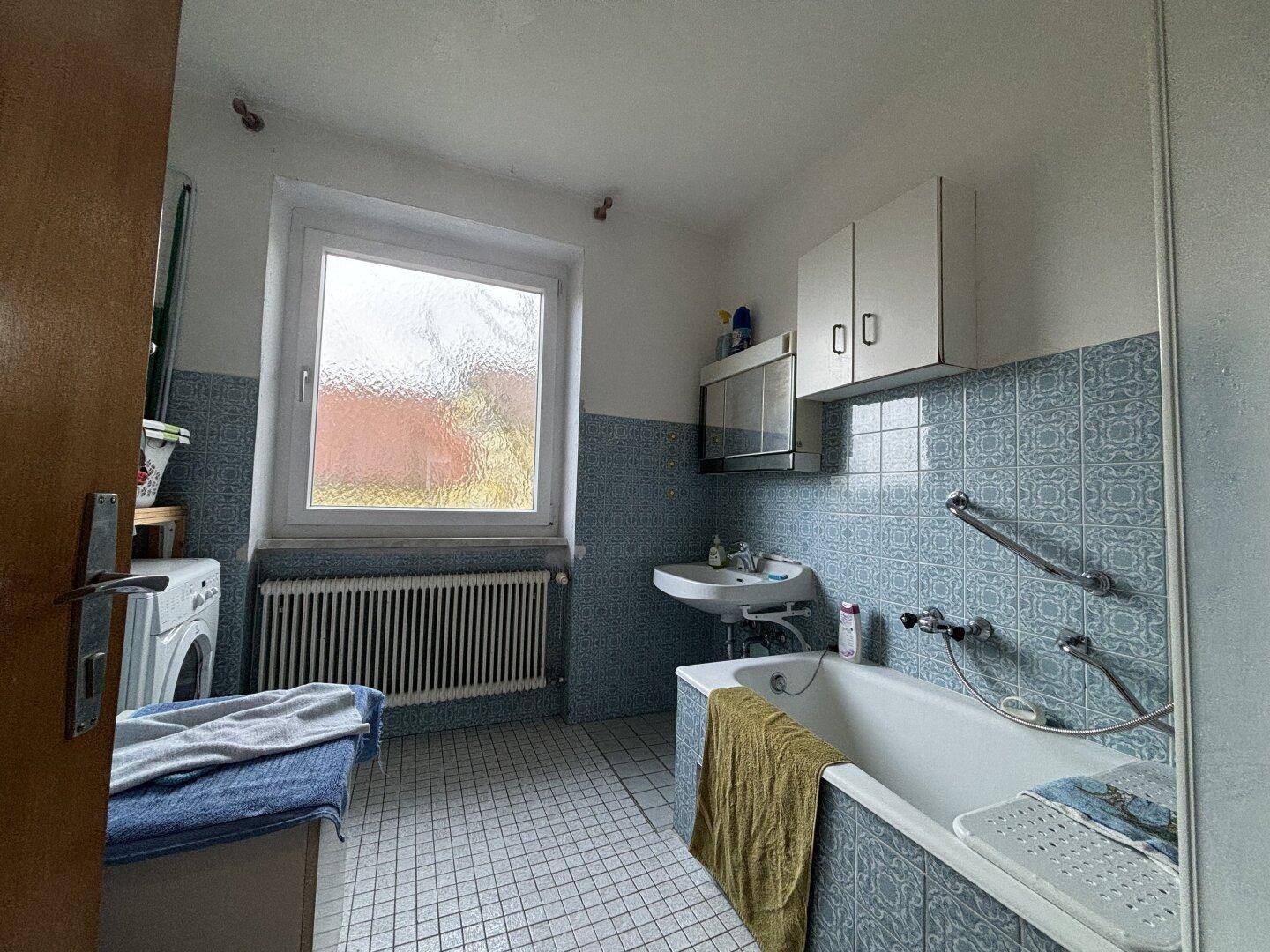 Badezimmer mit Badewanne, Waschbecken und blauen Fliesen im 80er-Jahre-Stil.