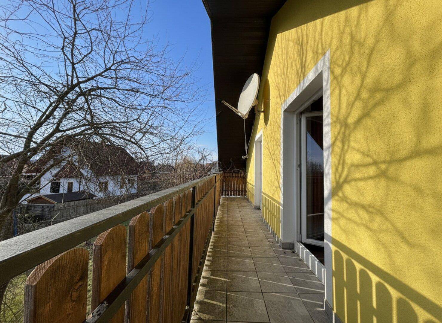 Langer Balkon mit Holzgeländer und Fliesenboden, der einen weiten Blick bietet.