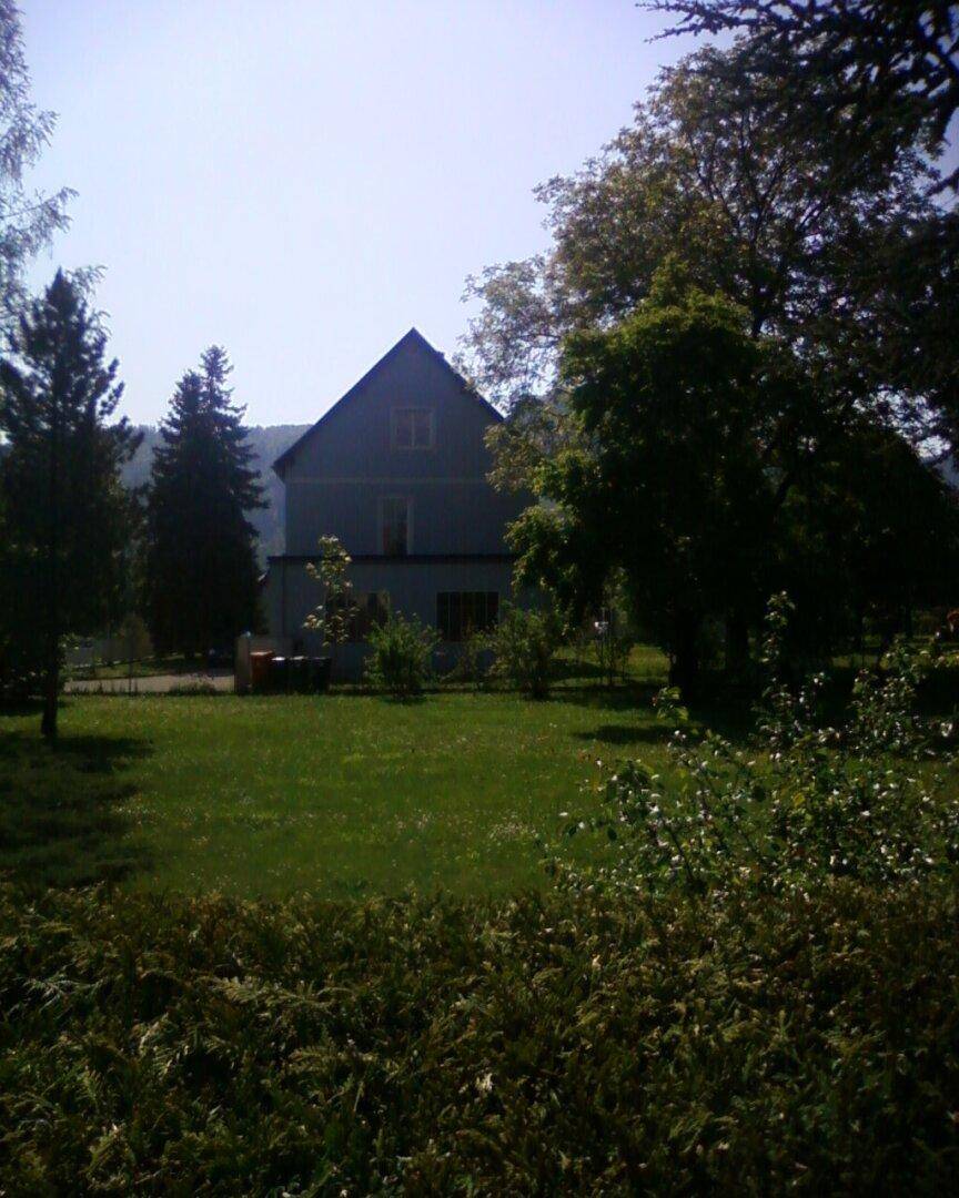 Weitläufige Grünfläche mit Bäumen und dem Wohnhaus, umgeben von Natur.