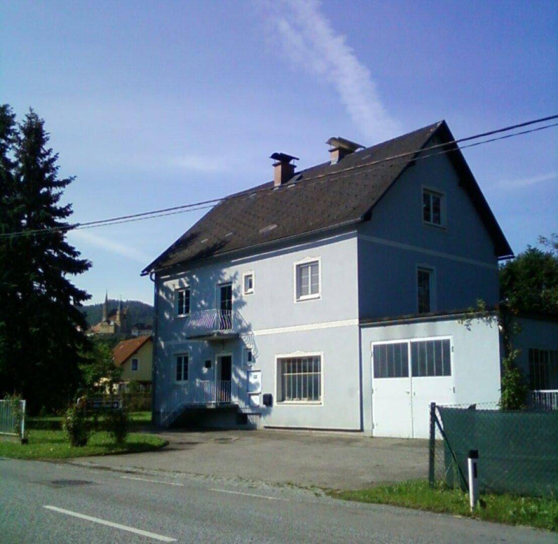 Wohnhaus mit hellblauer Fassade und Satteldach, umgeben von Bäumen und einer Straße.