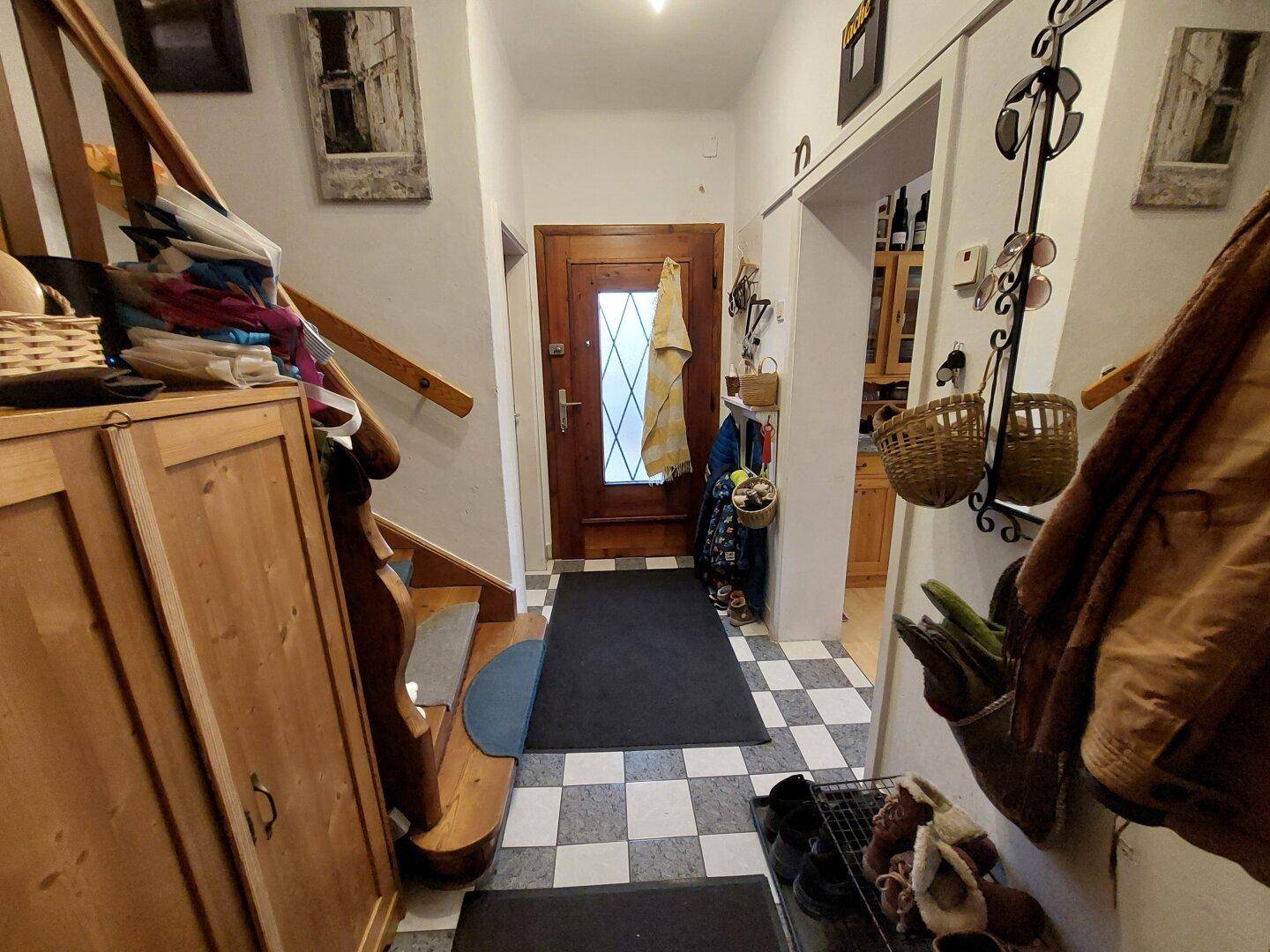 Eingangsbereich mit Holztreppe, Fliesenboden und Garderobe in traditionellem Stil.