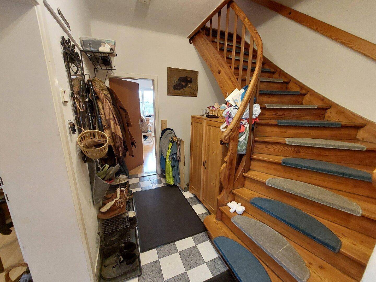 Heller Flur mit Holztreppe, Fliesenboden und praktischer Garderobenlösung.