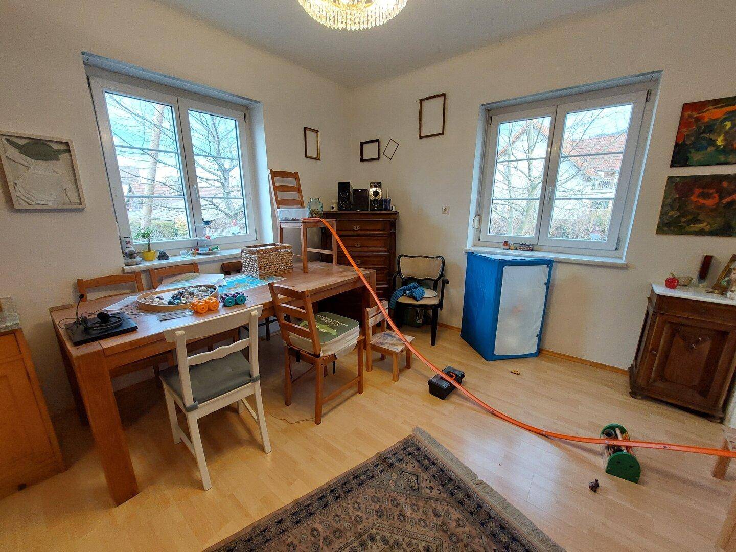 Essbereich mit Holztisch, Stühlen und Parkettboden, hell durch große Fenster.