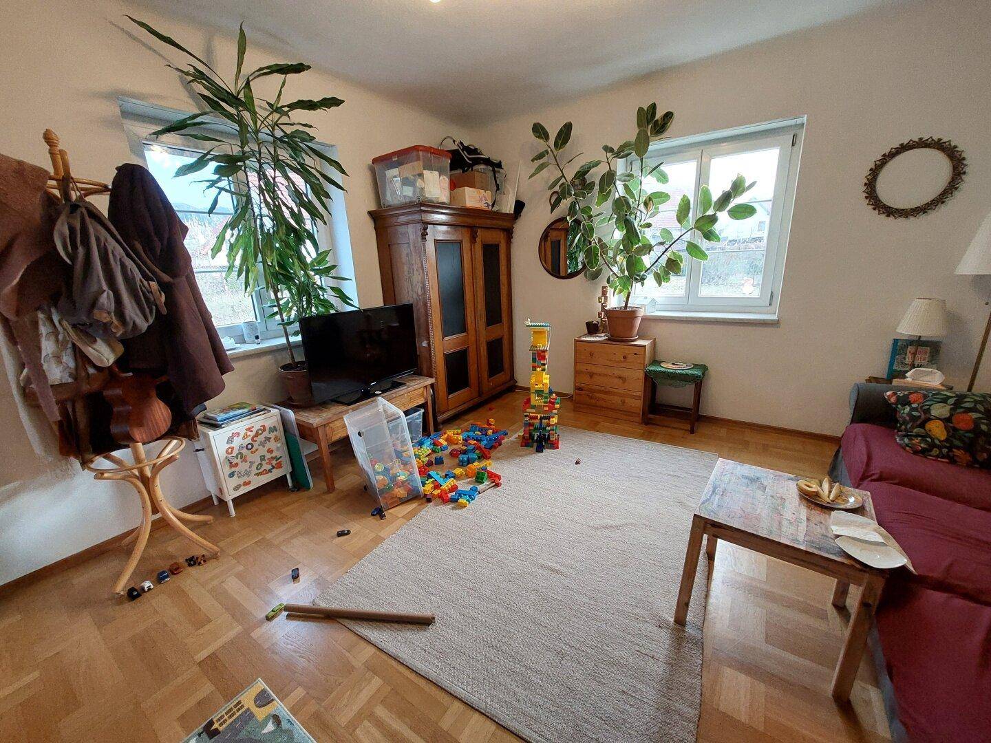 Gemütliches Wohnzimmer mit Parkettboden, Teppich und viel Tageslicht.