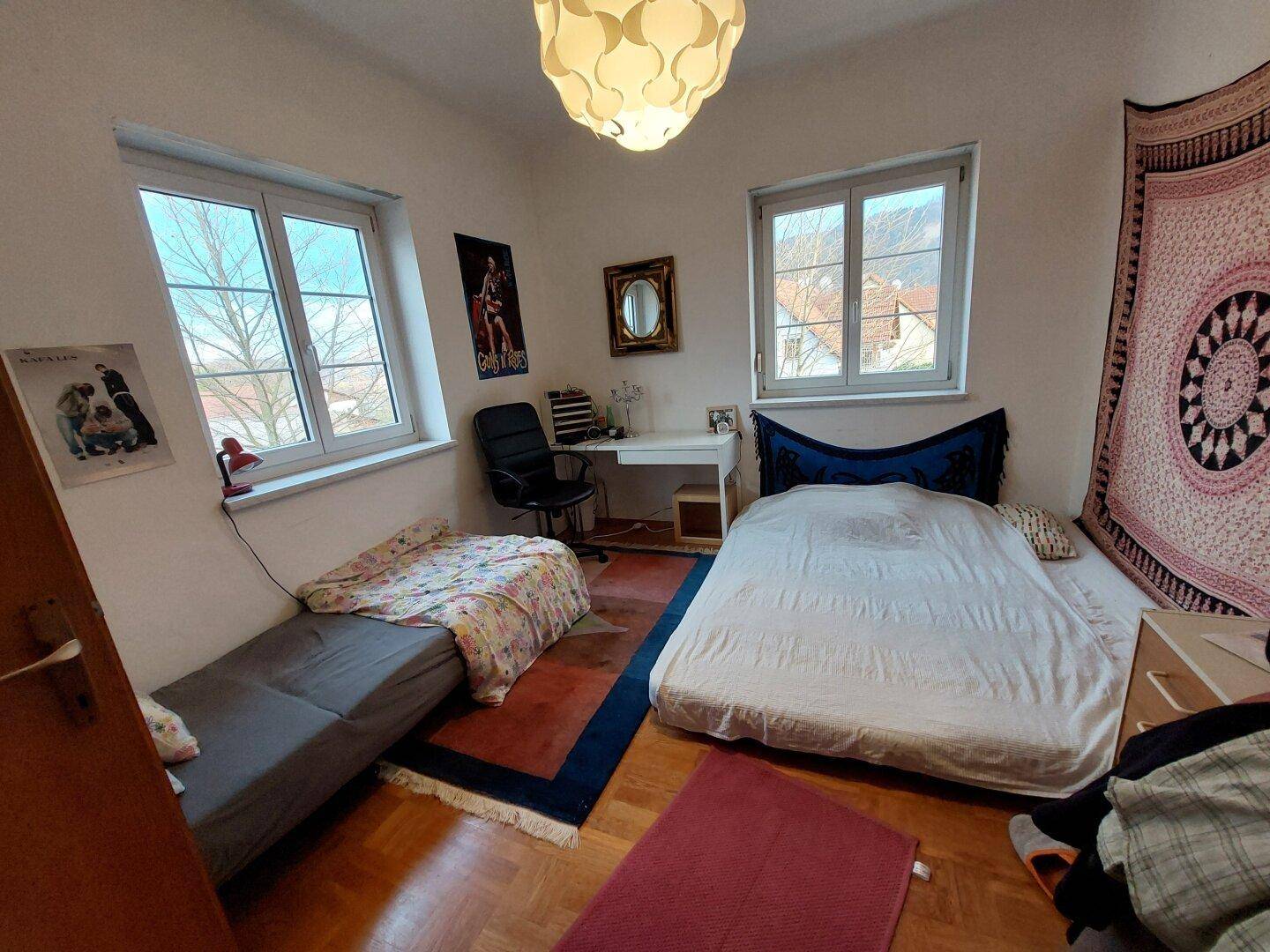 Schlafzimmer mit Parkettboden, zwei Fenstern und Platz für Bett und Schreibtisch.