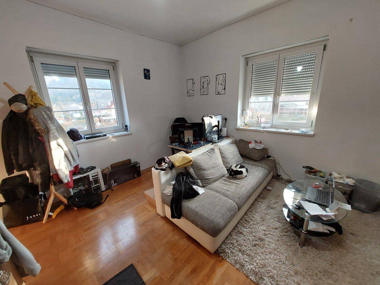 Wohnzimmer mit Parkettboden, Sofa und Fenster mit Rollläden.