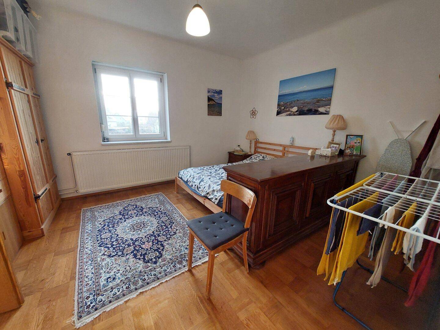 Schlafzimmer mit Parkettboden, großem Bett und traditionellem Teppich.