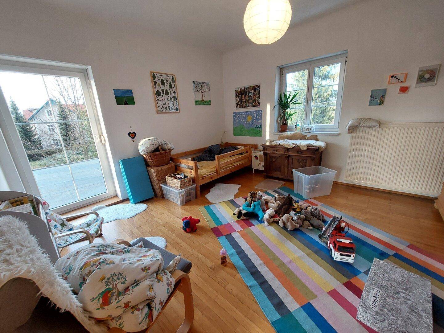 Kinderzimmer mit Holzboden, bunter Teppich und Zugang zum Außenbereich.