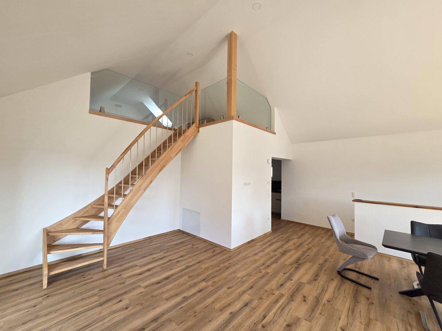 Elegante Holztreppe mit Glasgeländer führt zur oberen Galerie in einem hellen Wohnbereich.