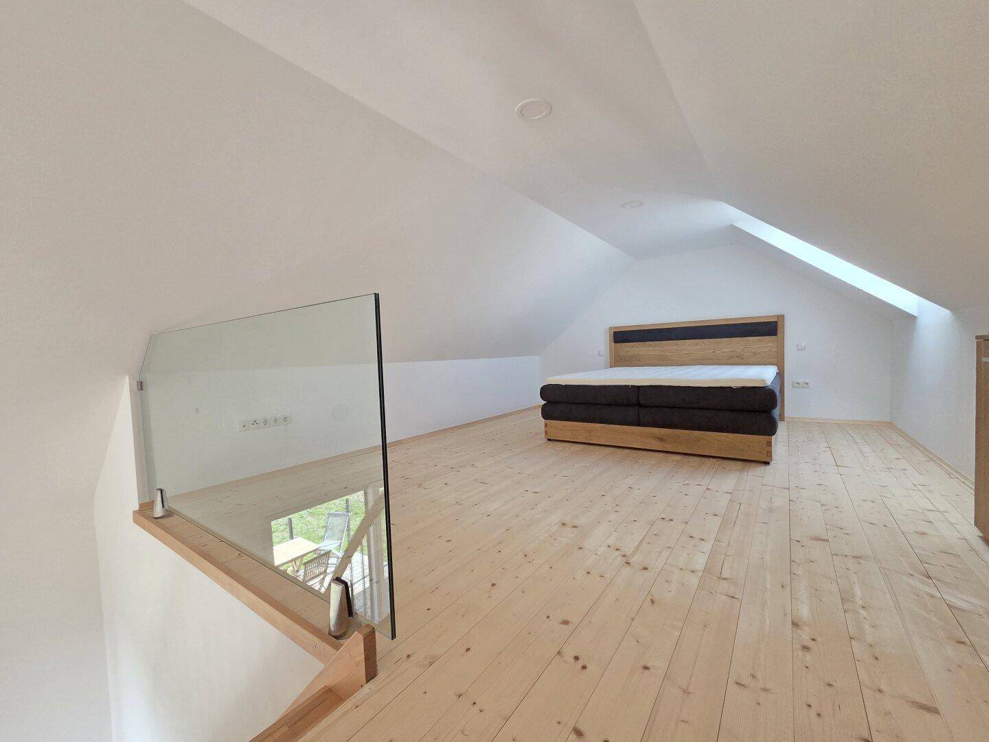 Helles Schlafzimmer auf der Galerie mit Holzboden, Dachschrägen und modernem Bettgestell.