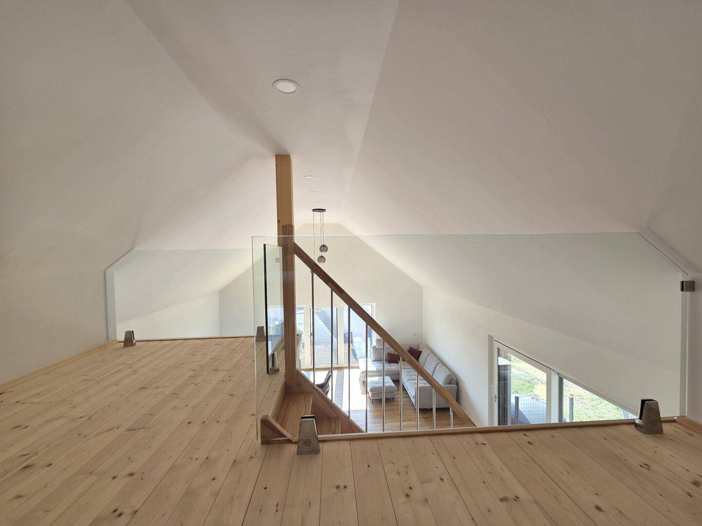 Blick von der oberen Galerie in den offenen Wohnbereich mit hohen Decken und großen Fenstern.