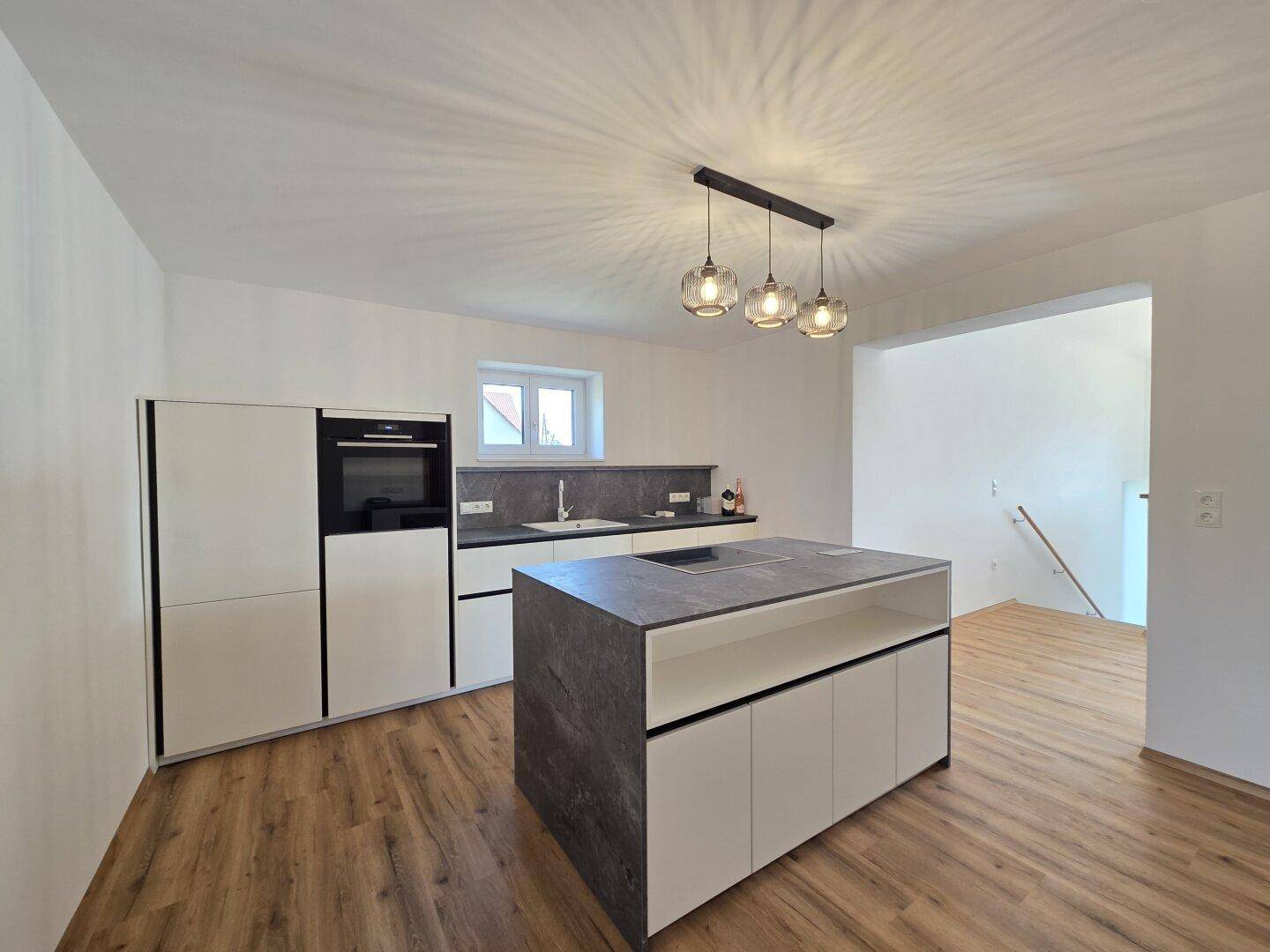 Moderne Küche mit Kücheninsel, integrierten Geräten und hellem Laminatboden in offenem Design.