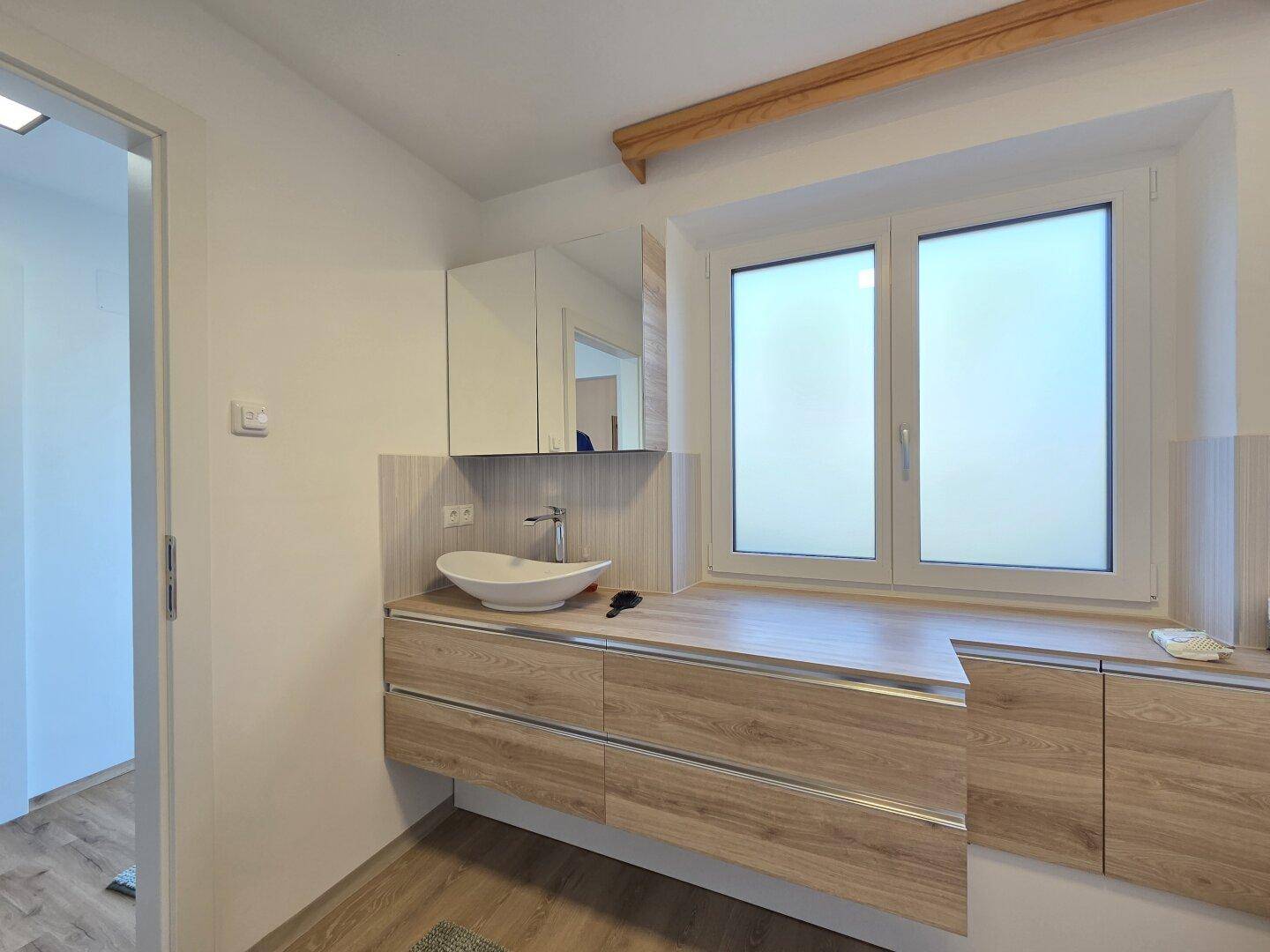 Helles Badezimmer mit modernem Waschtischunterschrank, großem Spiegel und Fenster.
