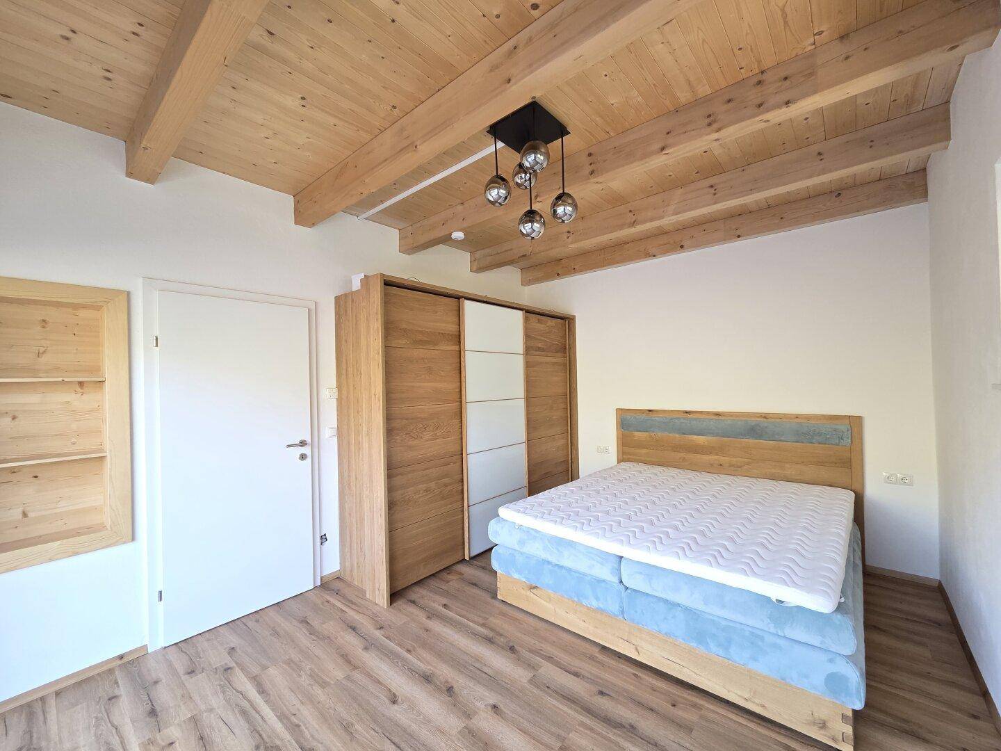 Gemütliches Schlafzimmer mit Holzbalkendecke, Laminatboden und modernem Kleiderschrank.