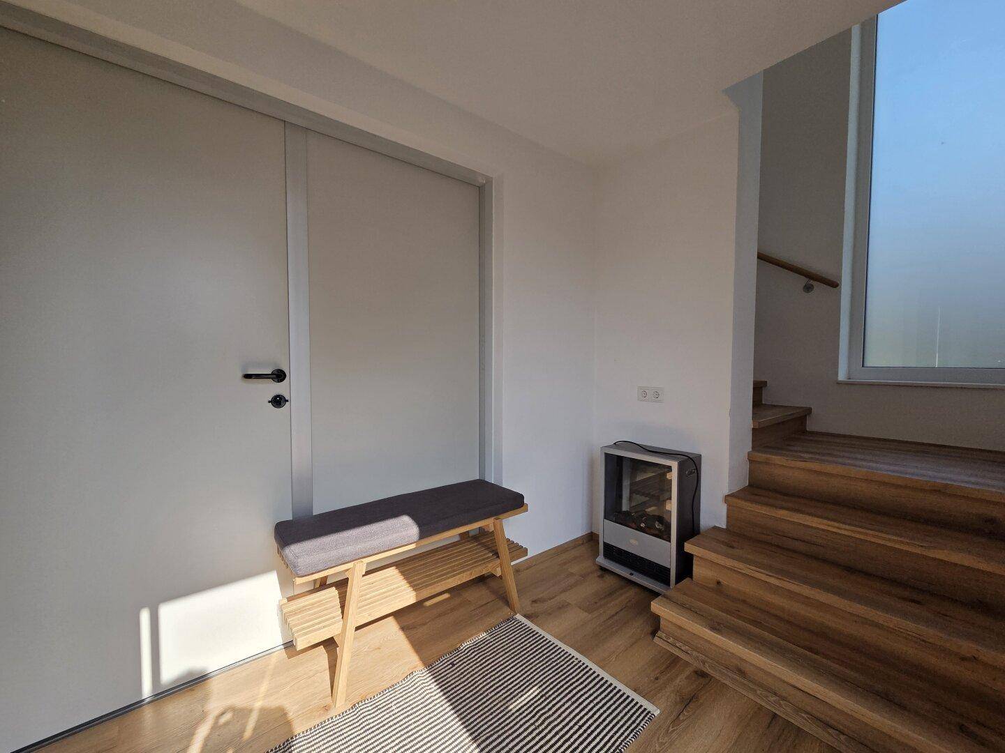 Eingangsbereich mit Holzboden, Sitzbank und einem modernen Holzofen für zusätzliche Wärme.