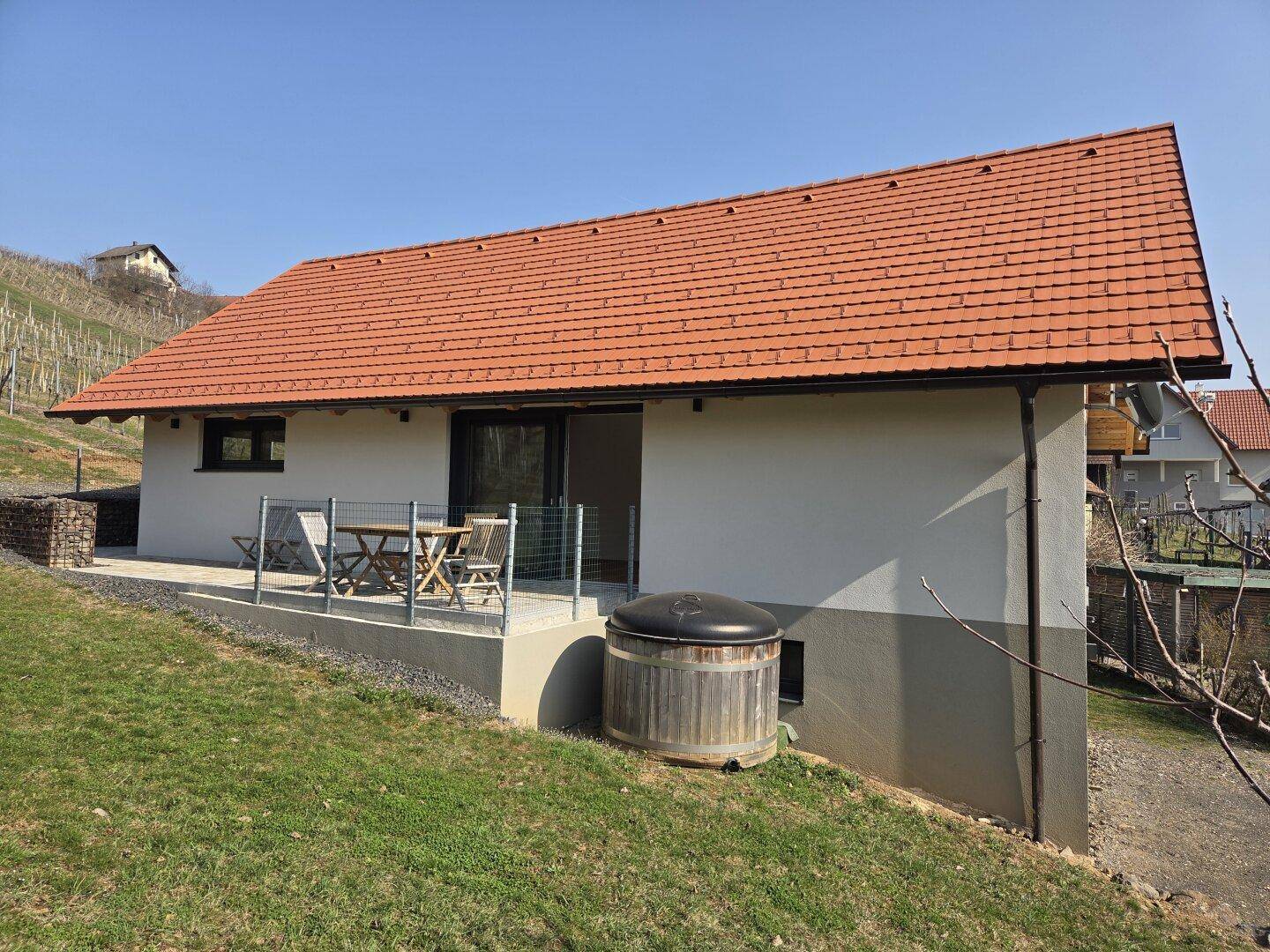 Rückseite des Hauses mit Terrasse, Sitzgelegenheiten und einem Holzbadezuber mit Blick auf die Weinberge.
