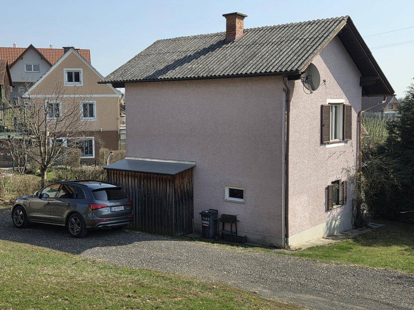 Rückansicht des Hauses mit geparktem Auto, Schuppen und Satellitenschüssel.