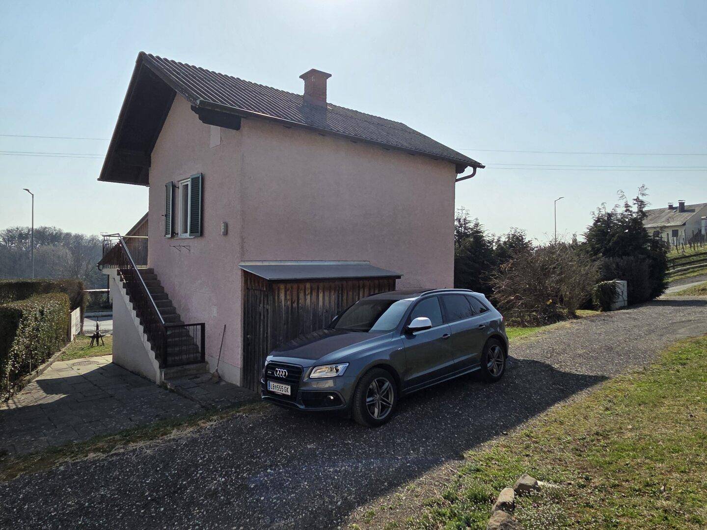 Seitenansicht des Hauses mit geparktem Auto und Schuppen auf dem Kiesweg.