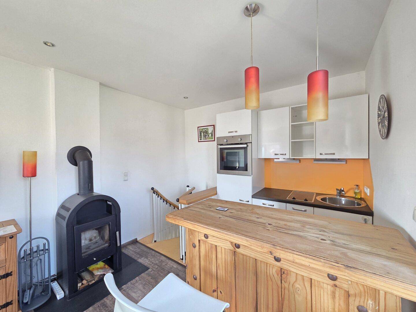 Funktionale Küche mit weißen Schränken, Holztheke und rustikalem Holzofen.