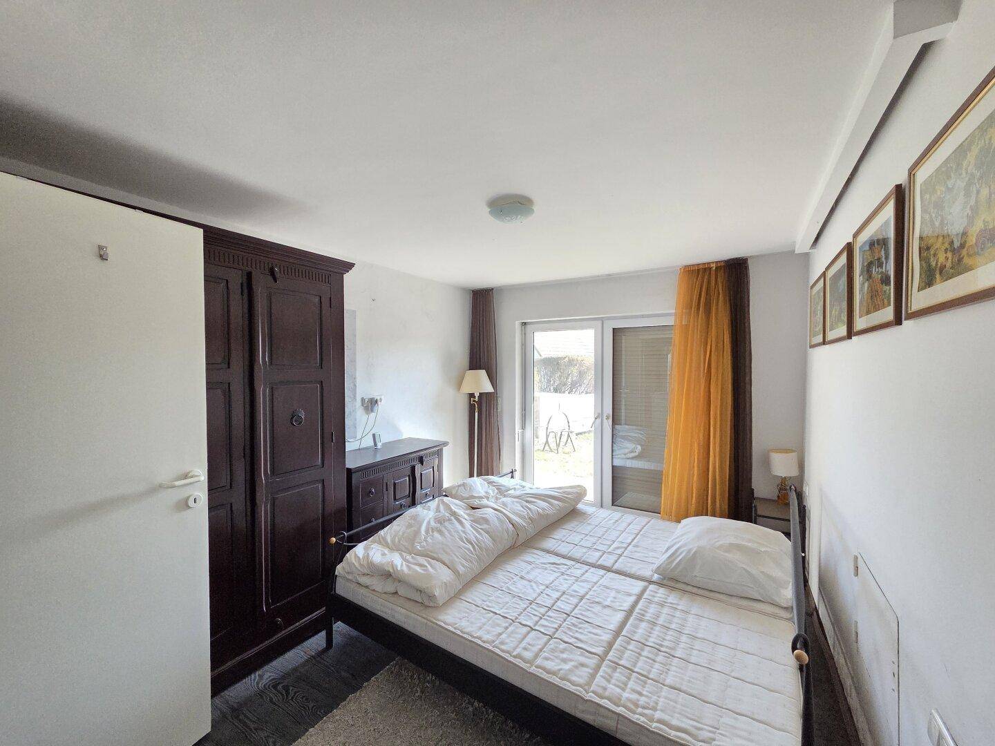 Schlafzimmer mit Doppelbett, dunklem Kleiderschrank und direktem Balkonzugang.