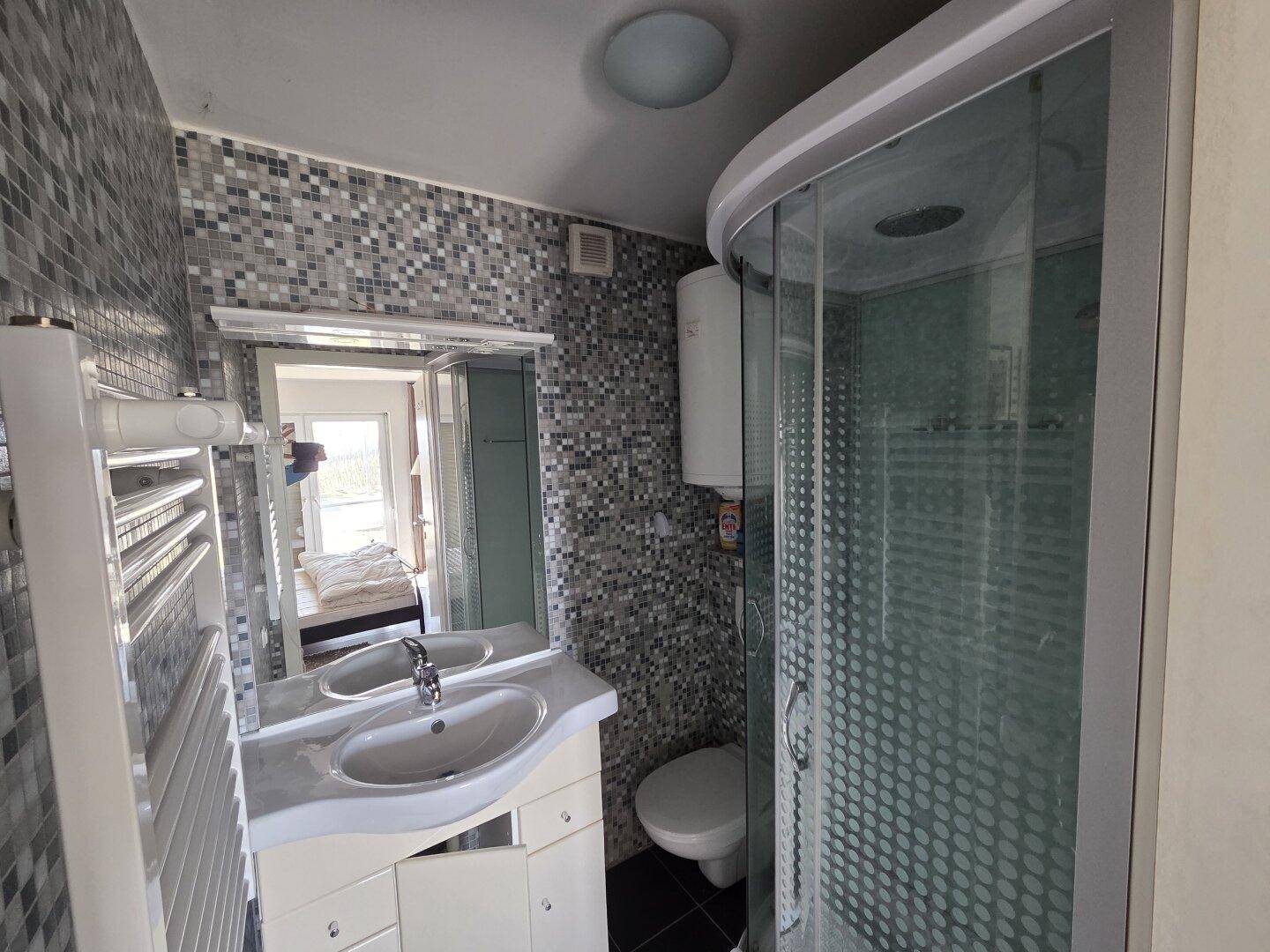 Modernes Badezimmer mit Duschkabine, Waschbecken und Mosaikfliesen an der Wand.