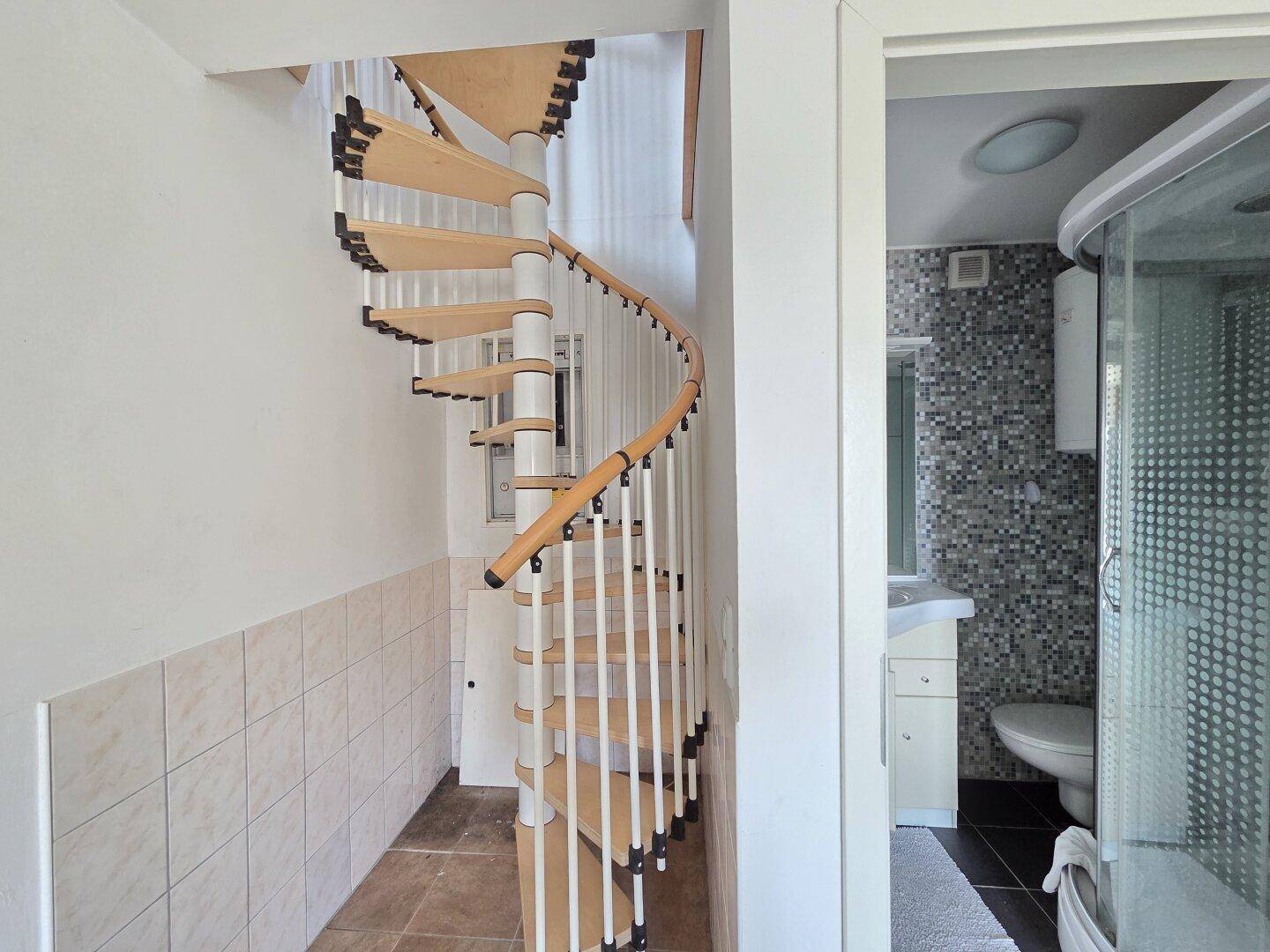 Wendeltreppe führt zu einem Badezimmer mit Mosaikfliesen und Duschkabine.