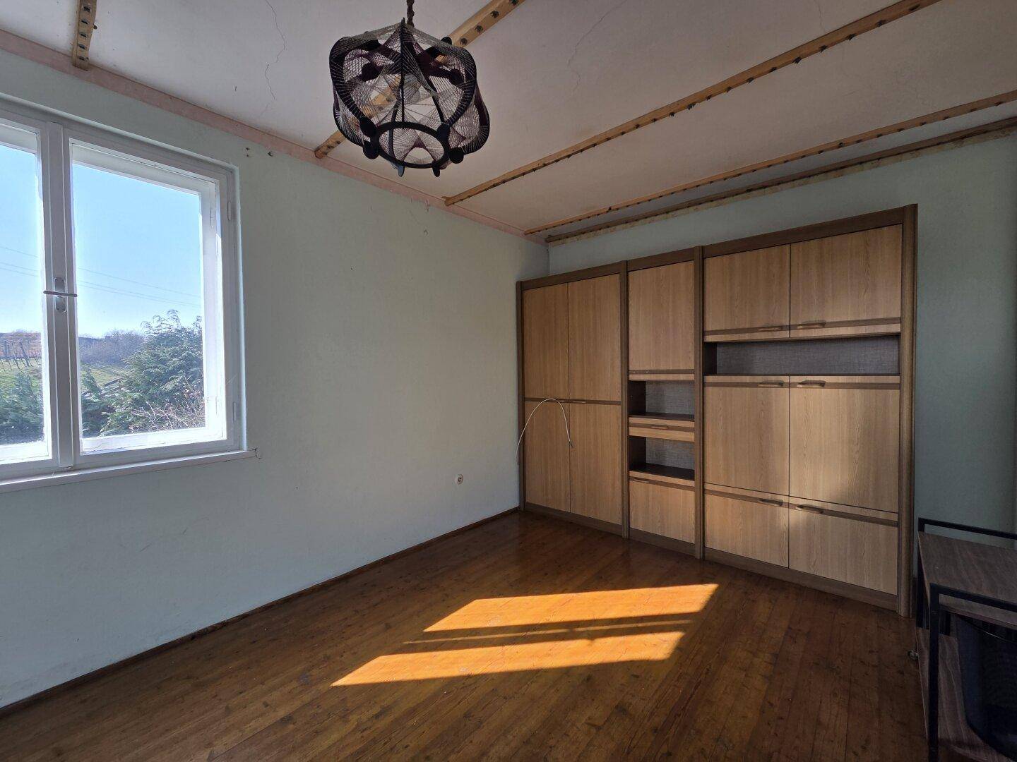 Helles Zimmer mit Holzboden, großen Fenstern und eingebauten Holzschränken.