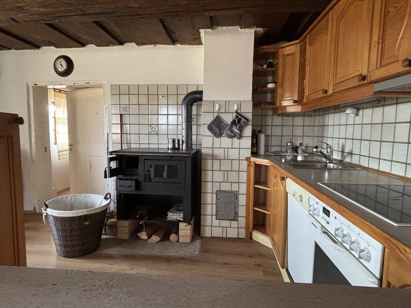 Rustikale Küche mit Holzschränken, Kachelofen und freiliegenden Deckenbalken.