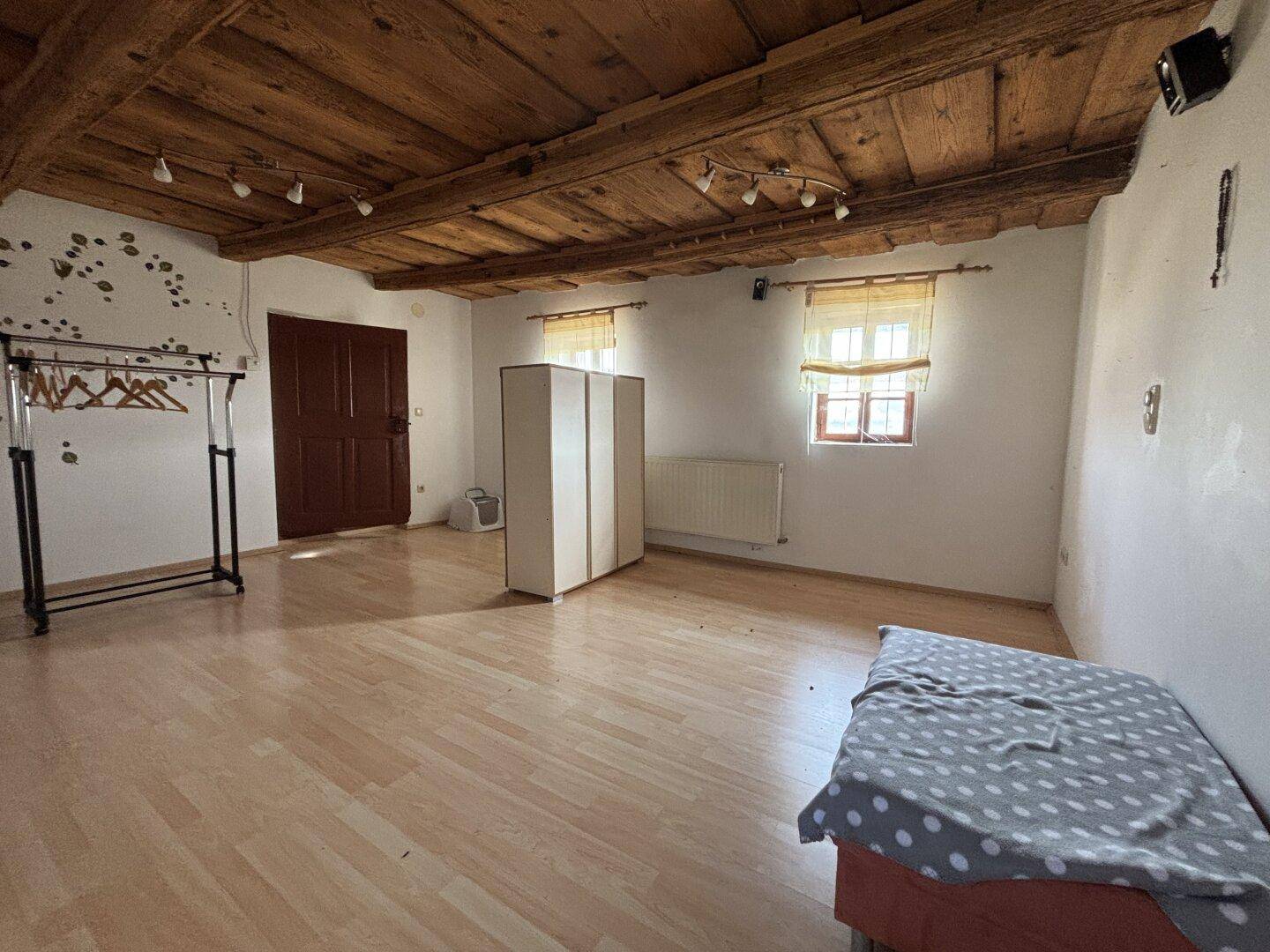 Helles Schlafzimmer mit Holzbalkendecke, Parkettboden und zwei Fenstern.