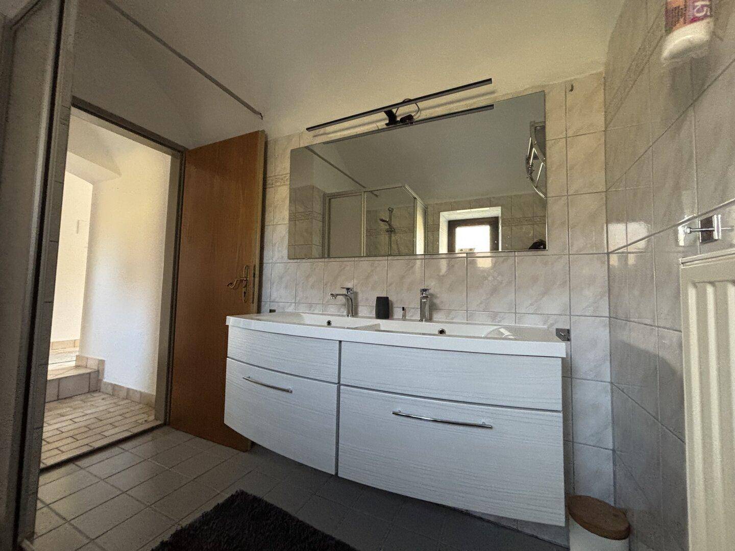 Modernisiertes Badezimmer mit Doppelwaschbecken, großem Spiegel und hellen Fliesen.