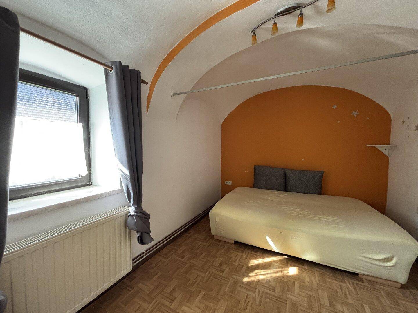 Schlafzimmer mit gewölbter Decke, farbiger Akzentwand und Parkettboden.