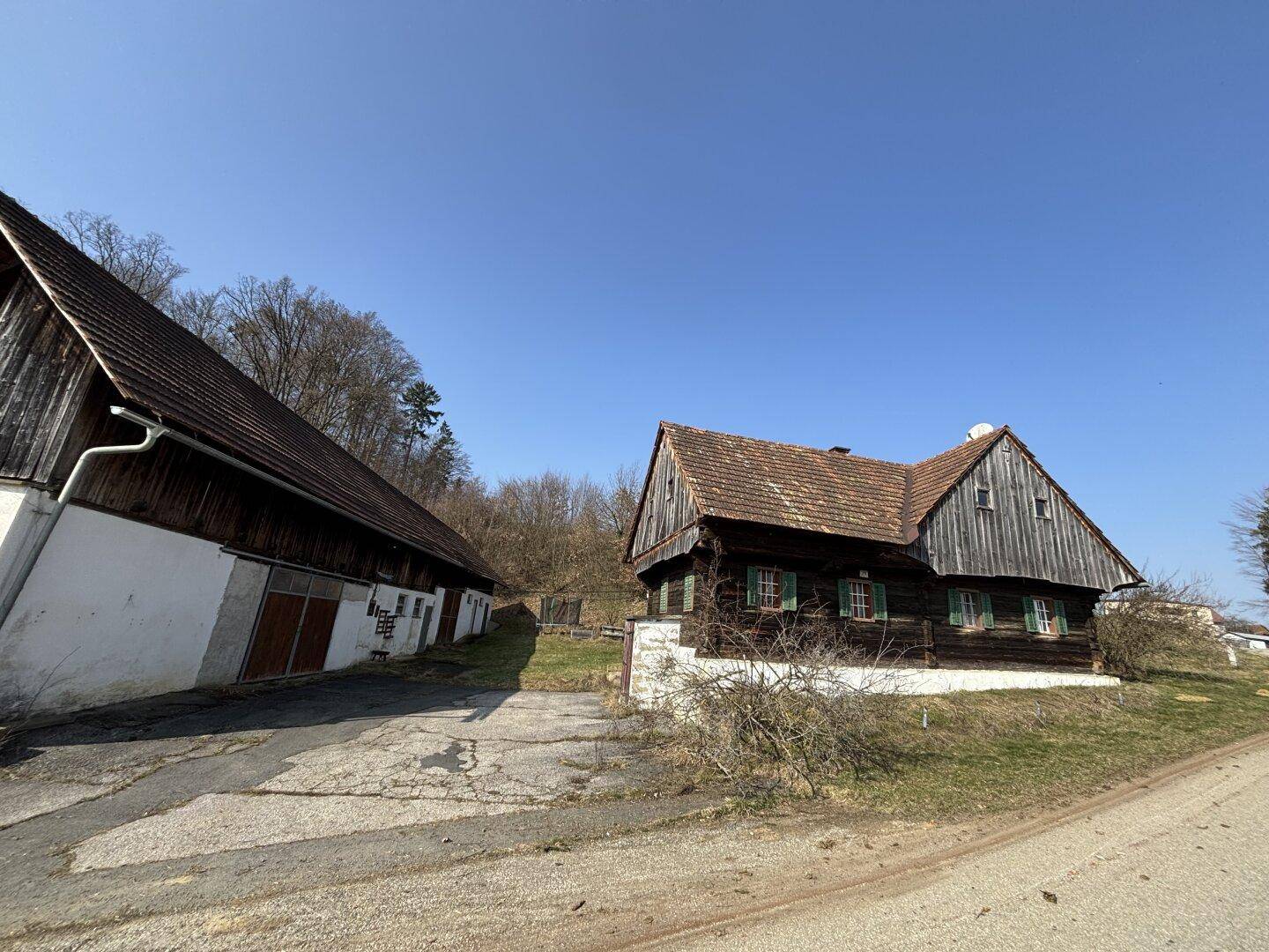 Ländliches Anwesen mit traditionellem Holzhaus und Nebengebäude unter blauem Himmel.