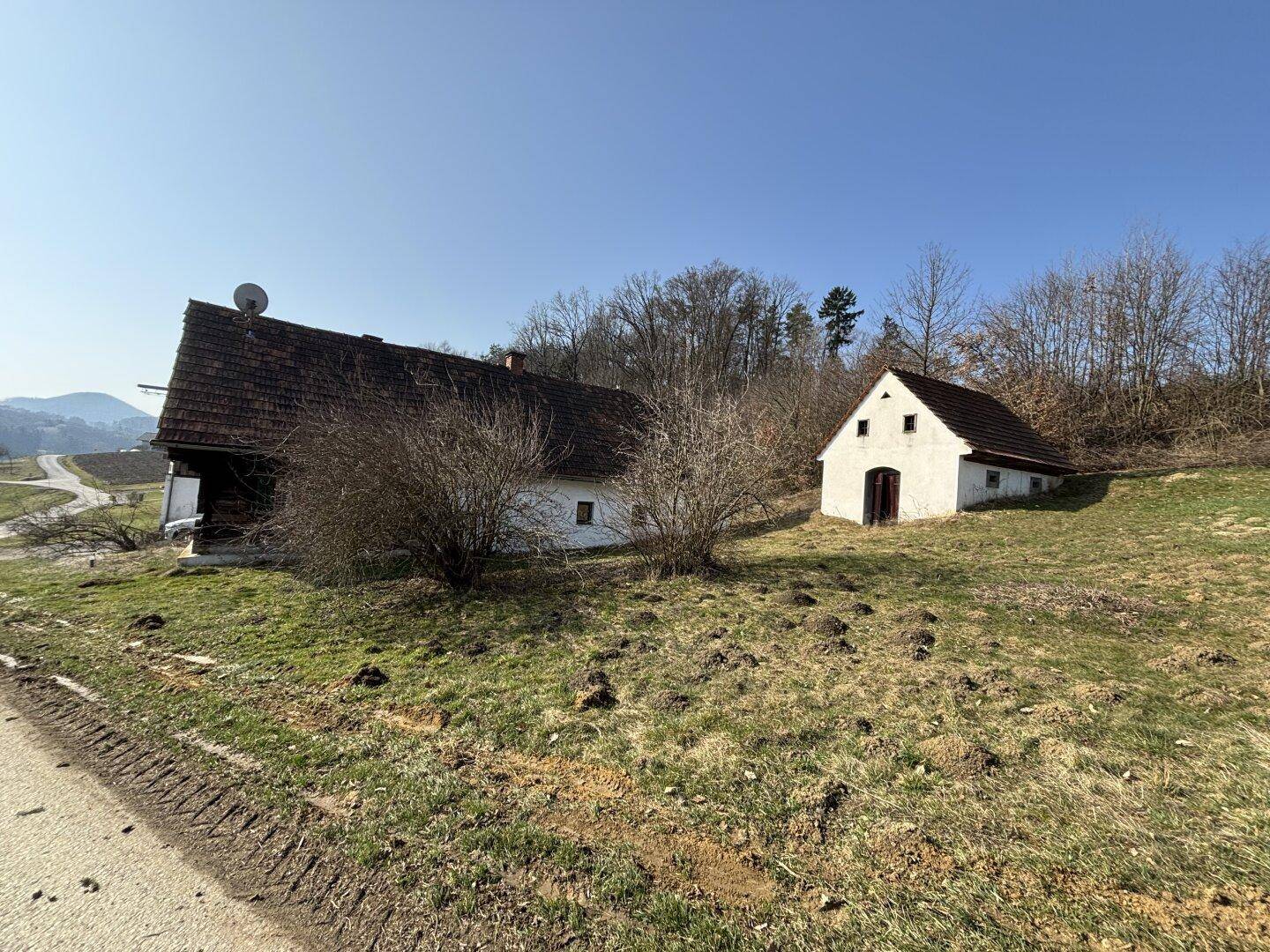 Anwesen mit Haupthaus und kleinem Nebengebäude in grüner Hügellandschaft.