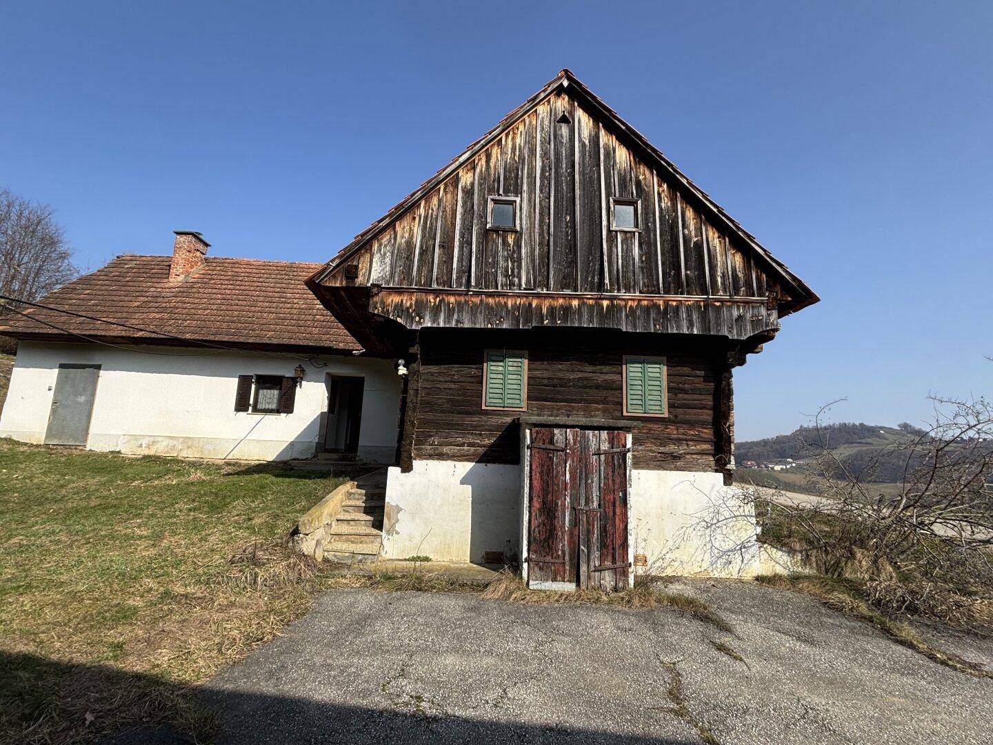 Traditionelles Holzhaus mit Satteldach, grünen Fensterläden und Nebeneingang.
