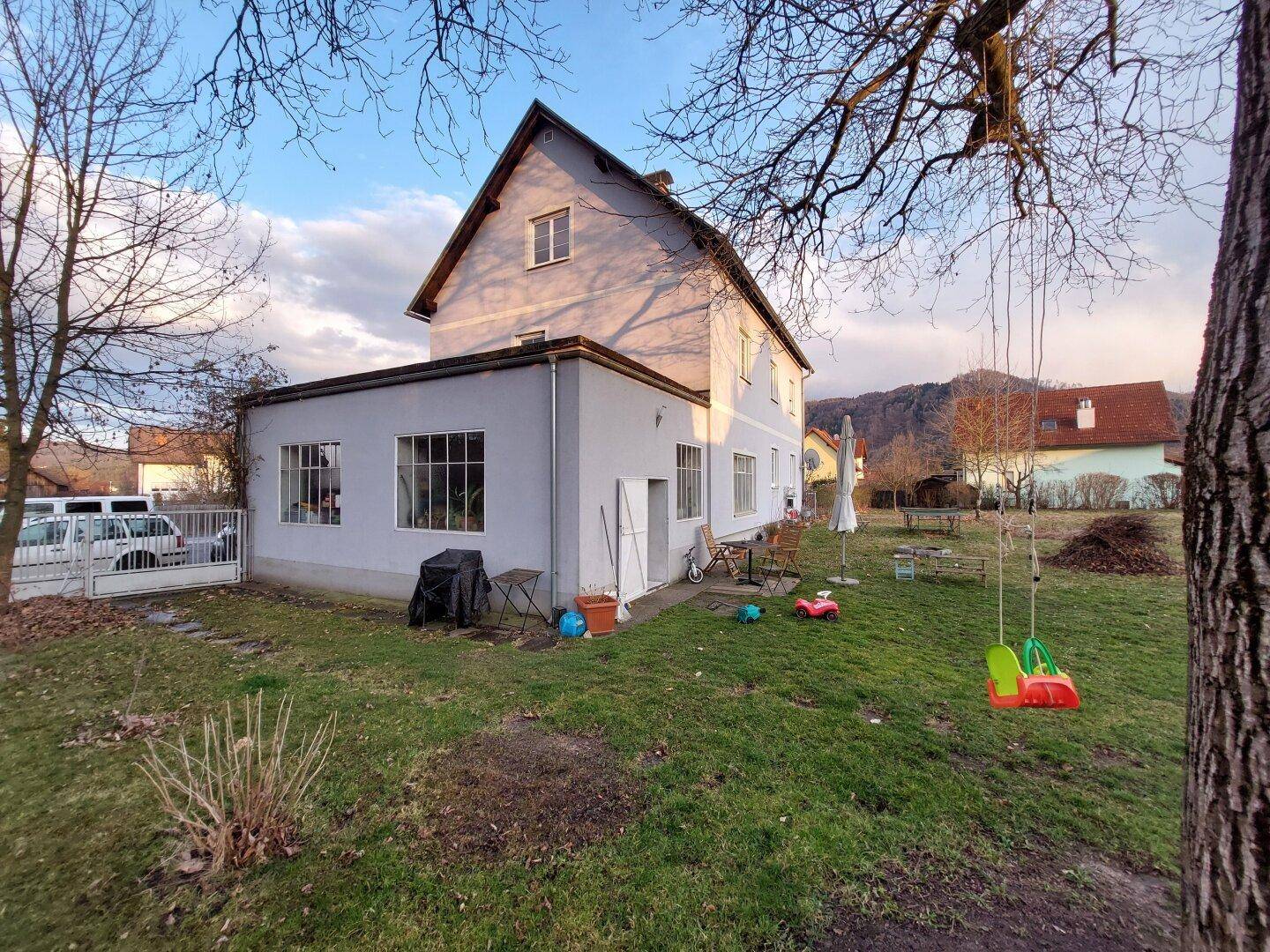Hinterhof mit Rasenfläche, Schaukeln und einem Anbau am Hauptgebäude.