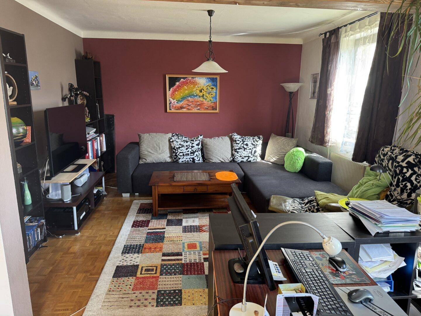 Gemütliches Wohnzimmer mit großem Ecksofa, Fernseher, farbenfrohem Teppich und Holzboden.