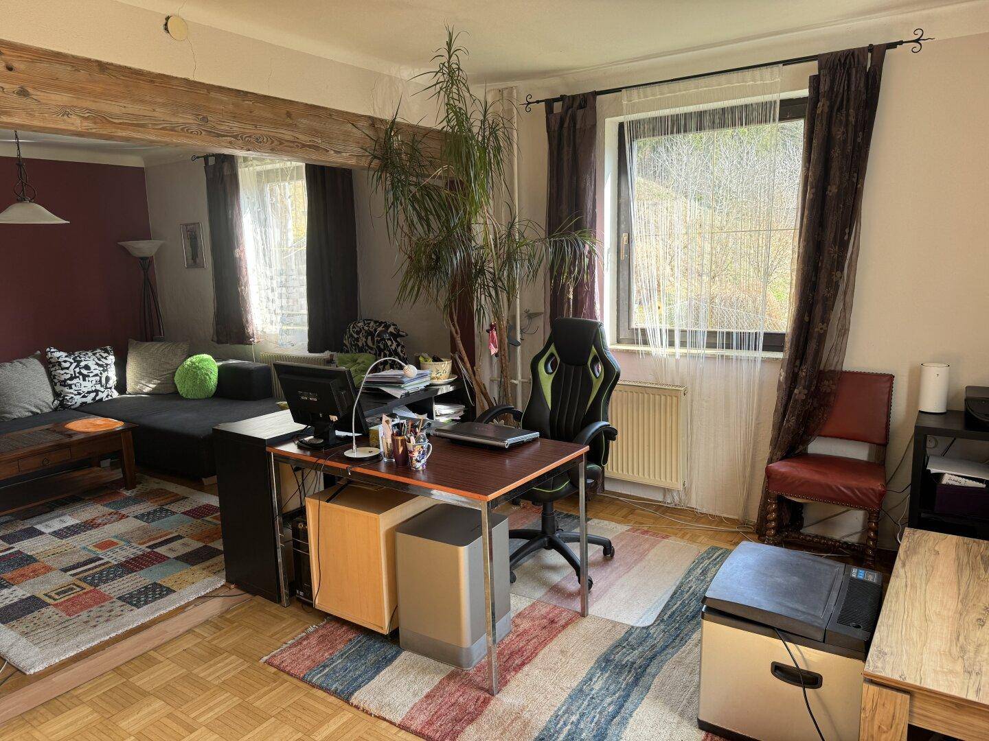 Heller Arbeitsbereich mit Schreibtisch, Bürostuhl, Holzbalken und Blick ins Grüne.