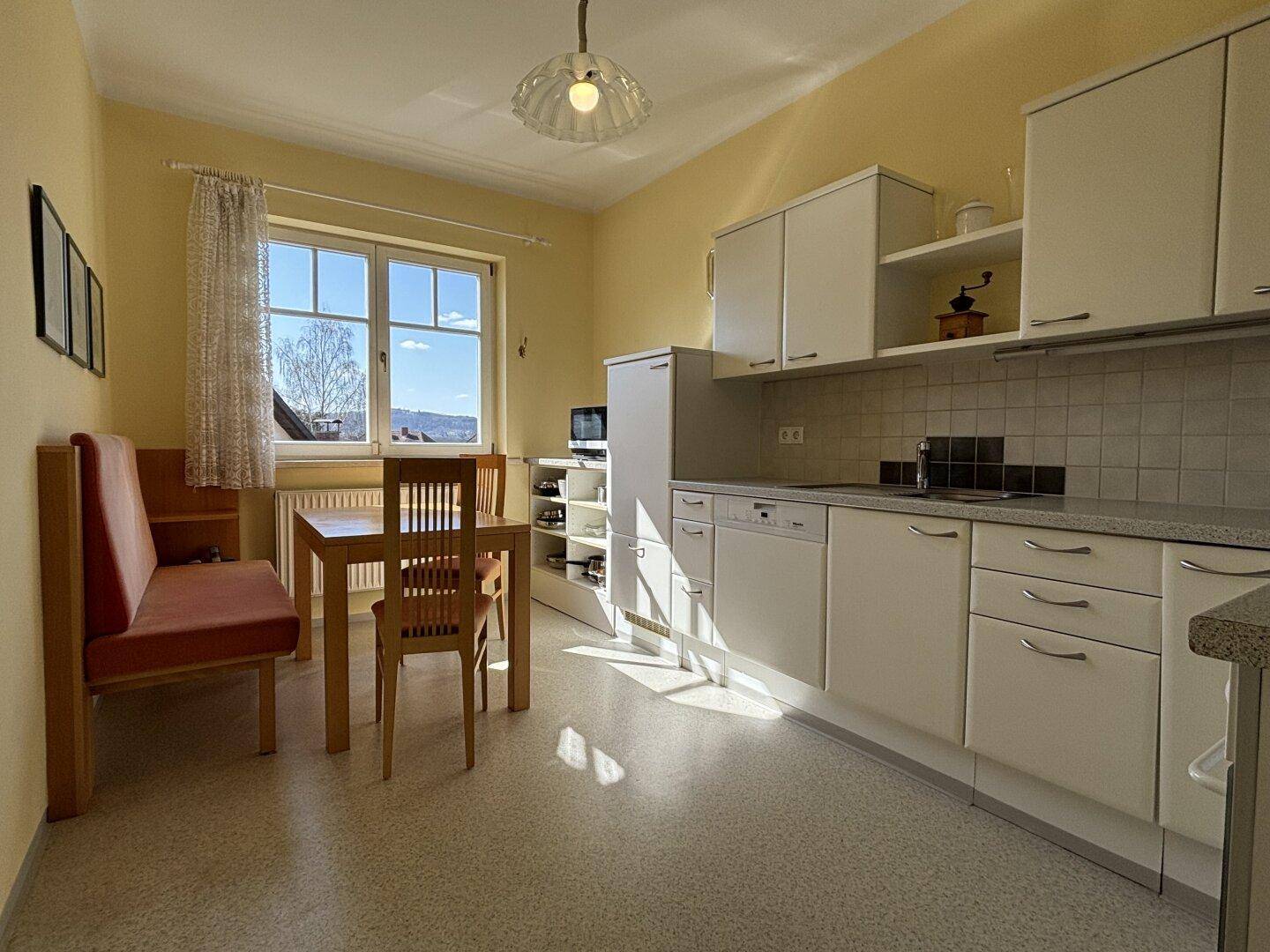 Funktionale Küche mit weißen Schränken, Essbereich und Fenster mit Ausblick.