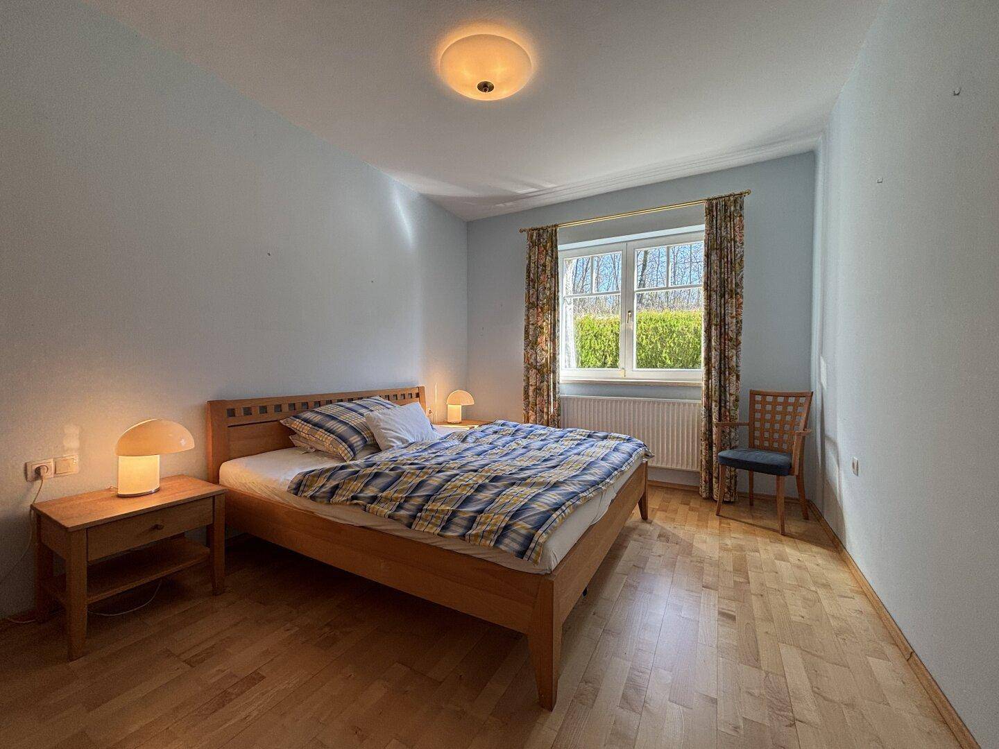 Gemütliches Schlafzimmer mit Holzbett, Nachttischen und Fenster mit Blick ins Grüne.