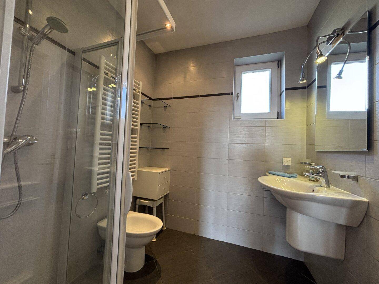 Modernes Badezimmer mit Dusche, WC, Waschbecken und Fenster für Tageslicht.