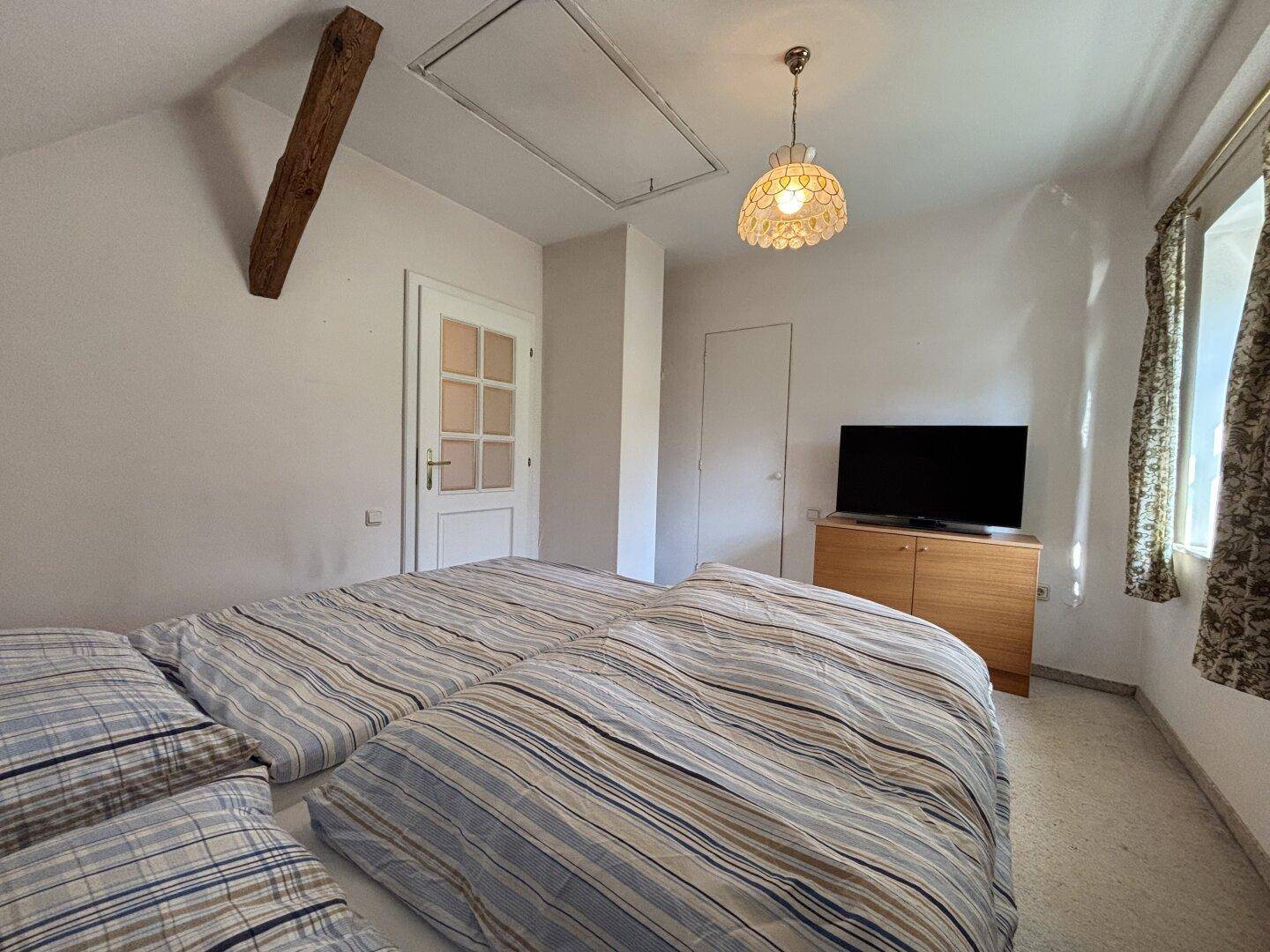 Gemütliches Schlafzimmer im Dachgeschoss mit Doppelbett, Fernseher und sichtbarem Holzbalken.