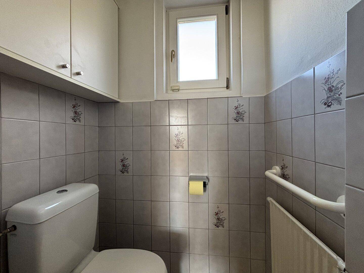 Helles Gäste-WC mit Fenster, WC und dekorativen Fliesen an den Wänden.